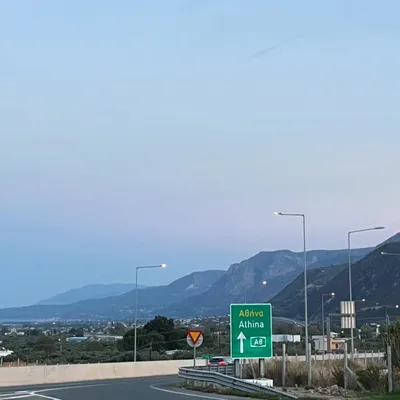 A highway sign pointing toward Athens on the A8, with mountains in the dusk sky