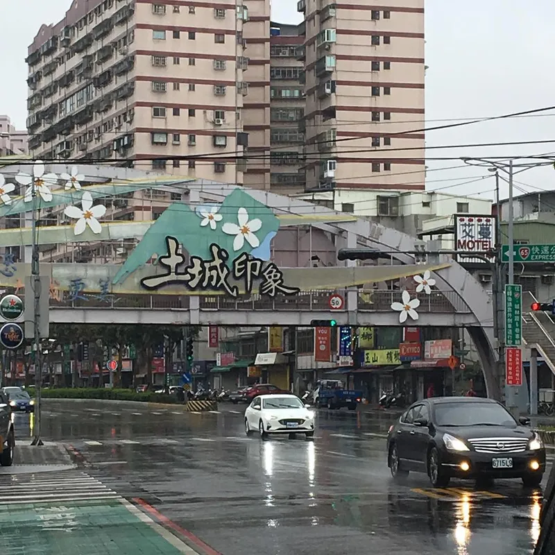 A rainy Taiwanese street intersection with a decorative arch bearing Chinese characters