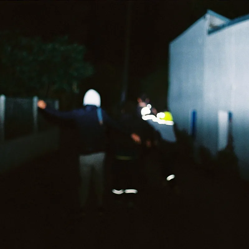 A blurry night shot of a person in a hoodie walking past a lit building
