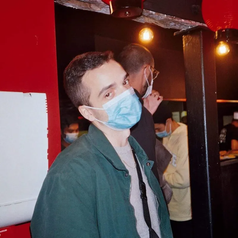 A man wearing a surgical mask looking back over his shoulder in a red-lit venue