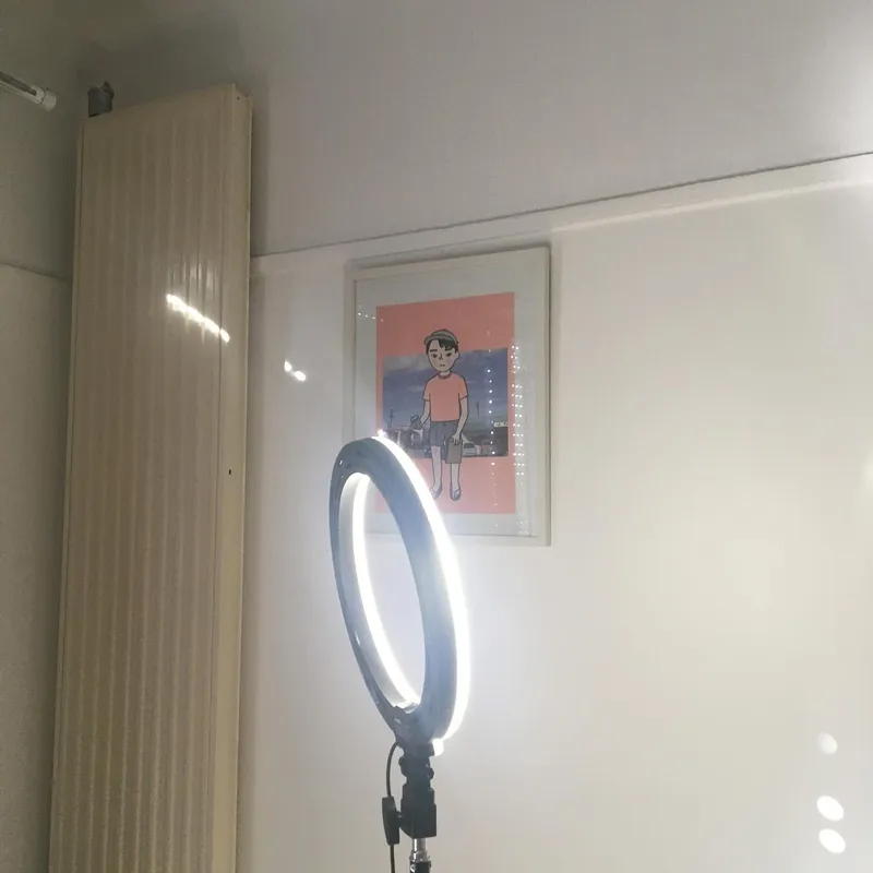 A ring light in a bedroom with an illustrated poster of a sad boy on the wall