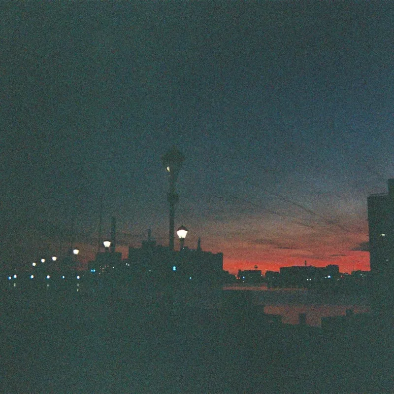 Dark cityscape at dusk with a vivid red-orange sunset and glowing street lamps
