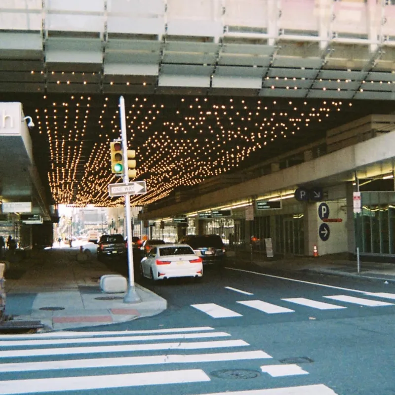 City street passing under an overpass adorned with rows of warm string lights