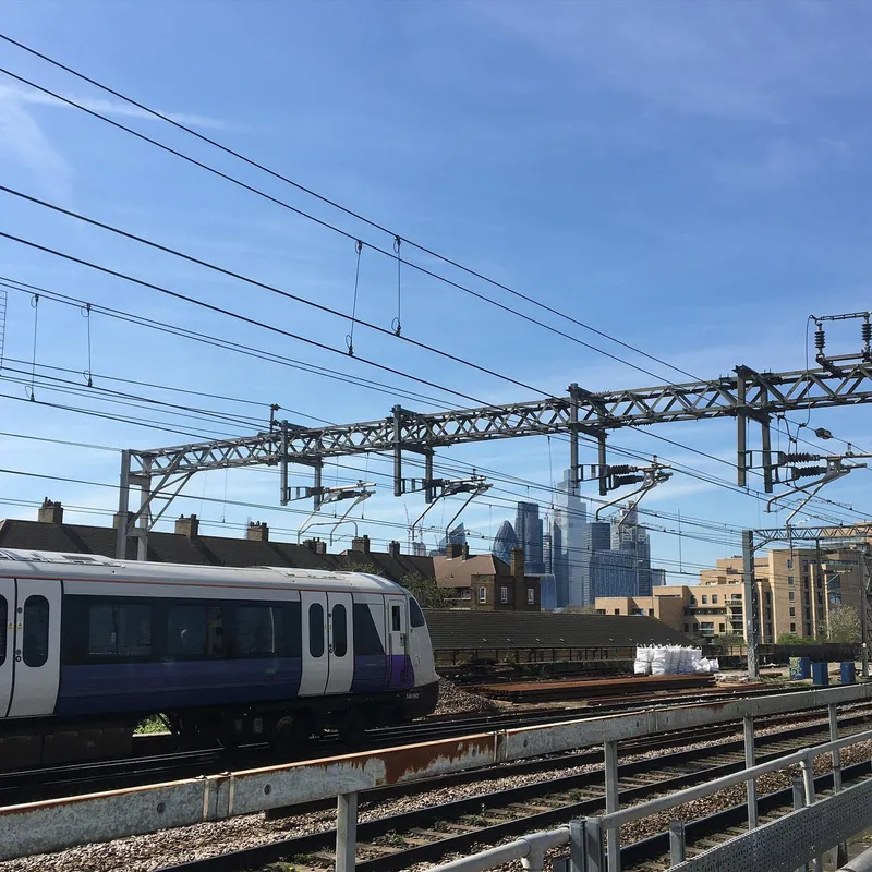 An city train on tracks with the City of London skyline behind it