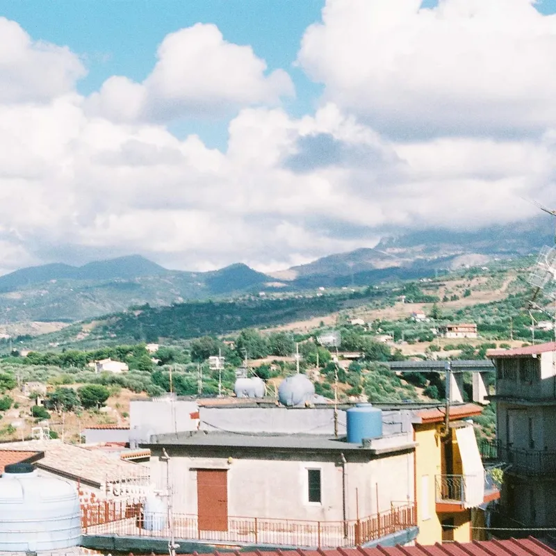 Rooftops and antennas with green hills and mountains behind a small Italian town