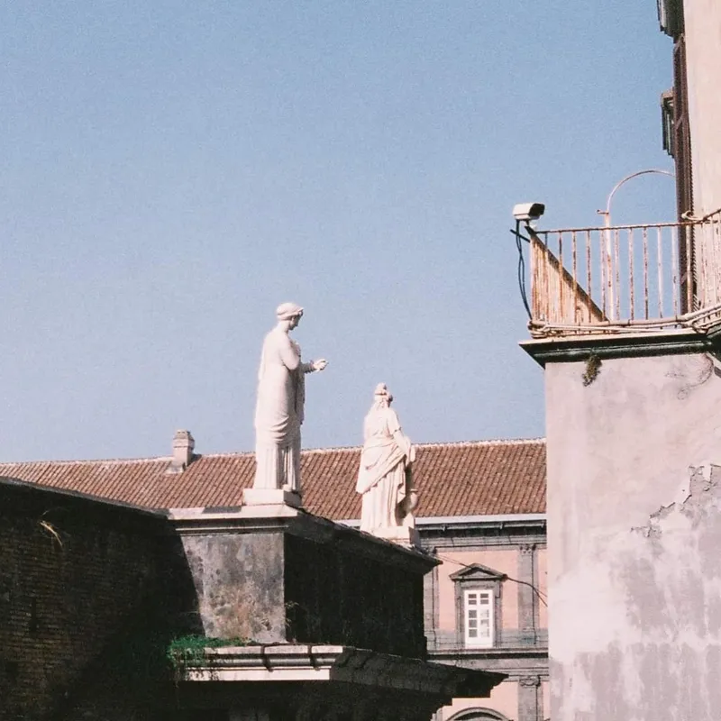 Two classical statues on a rooftop against a clear blue sky in Naples