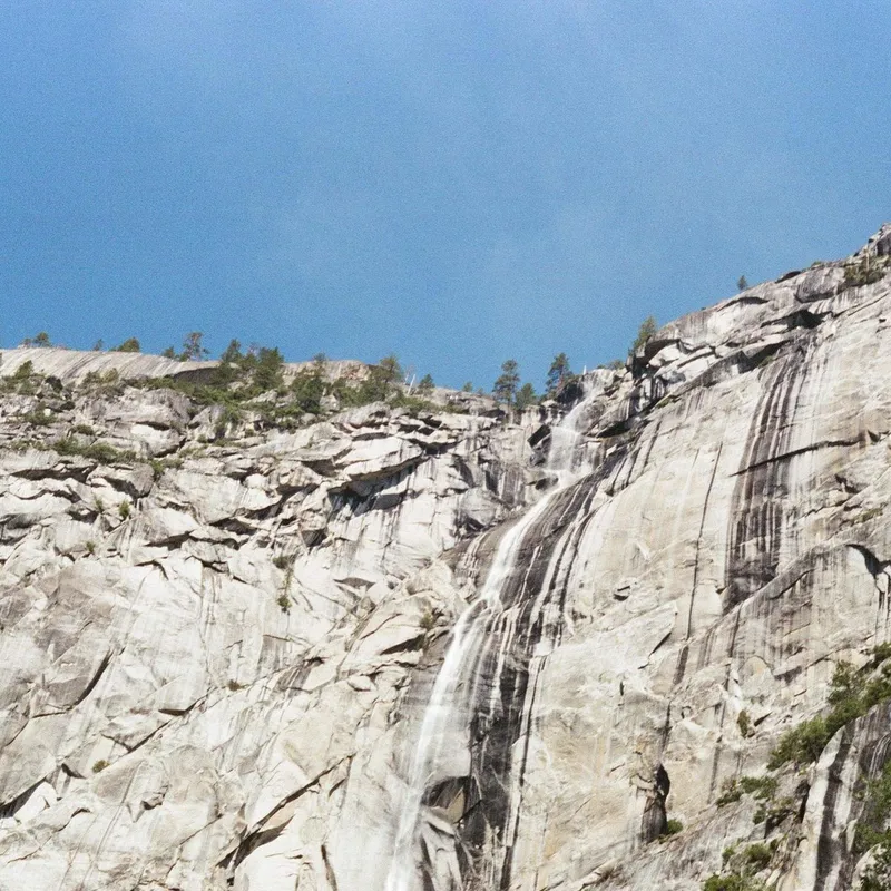 A thin waterfall streaking down a sheer granite cliff face against a blue sky