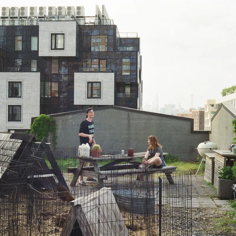 Two people chatting at a picnic table on a Brooklyn rooftop with the skyline behind them
