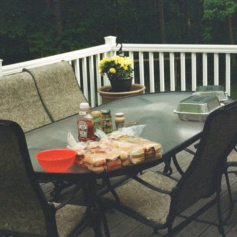 A backyard deck table set up with hot dog buns and condiments