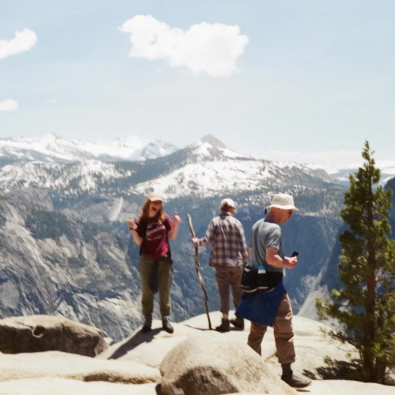 Three hikers on a rocky summit with snow-capped mountains stretching behind them