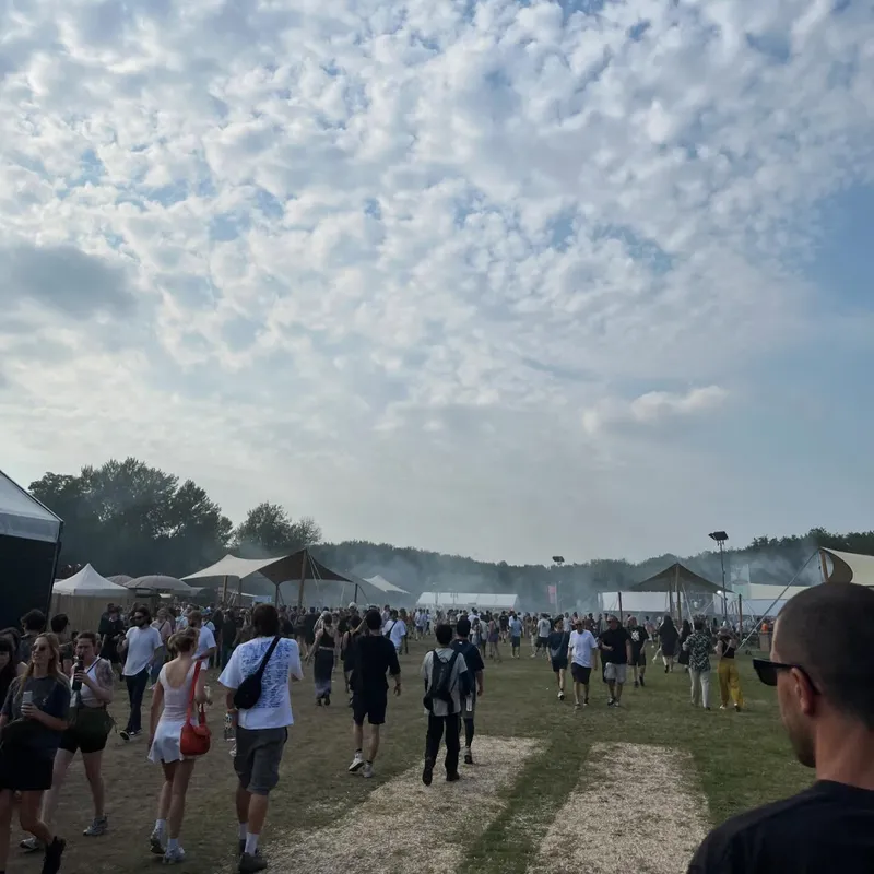 Festival grounds with crowds walking between tents under a cloudy sky
