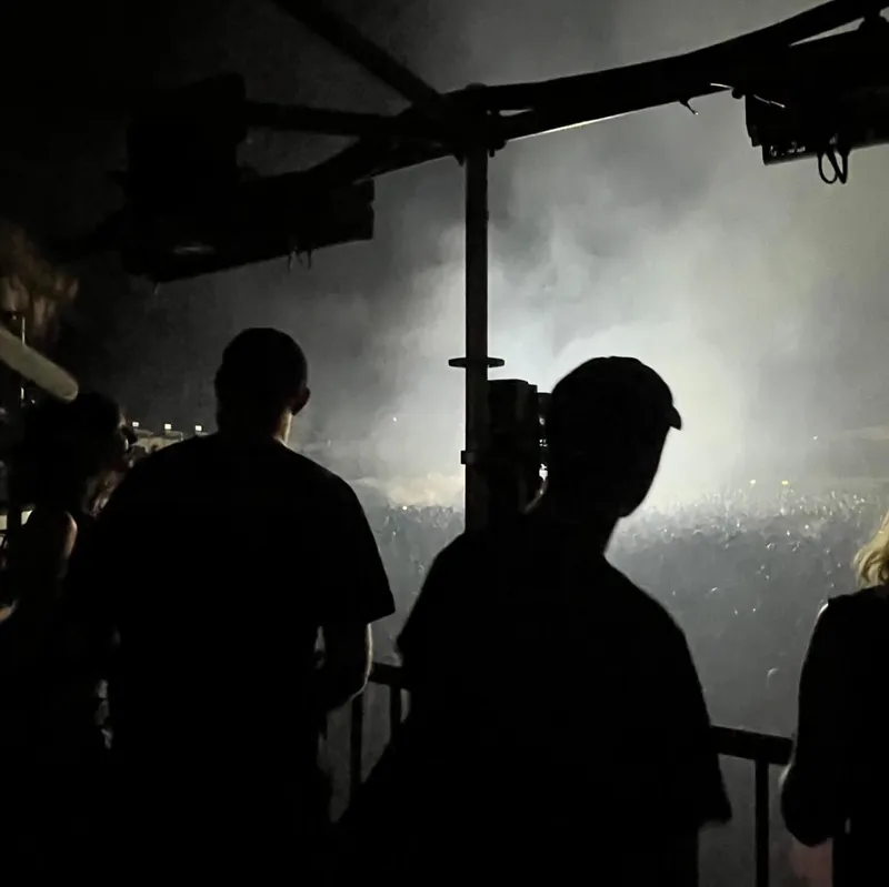 Silhouettes of people watching a smoky outdoor concert stage at night