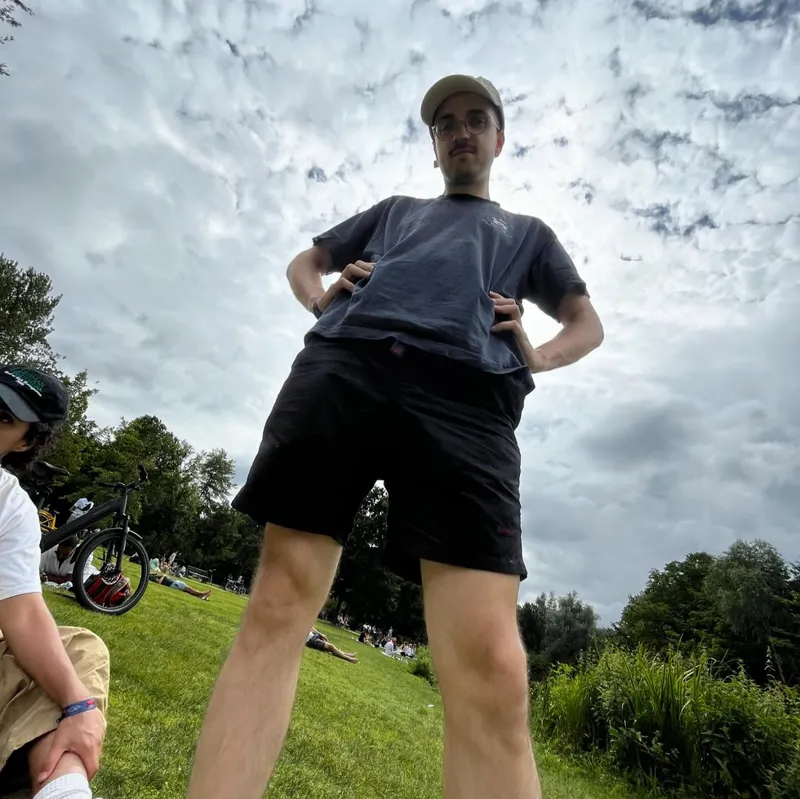 A fish-eye shot of someone standing in a park with a dramatic cloudy sky above