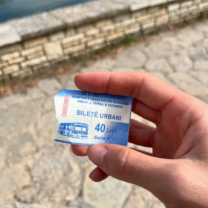 A hand holding an Albanian bus ticket