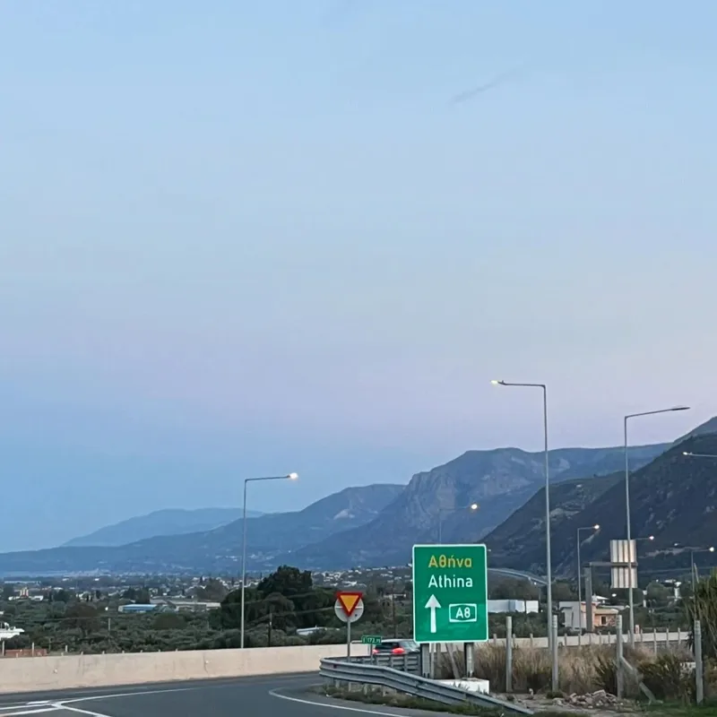 A highway sign pointing toward Athens on the A8, with mountains in the dusk sky