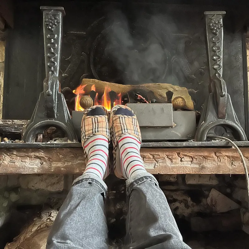Feet resting near a lit fireplace