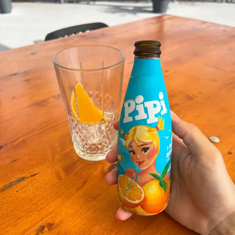 A hand holding a Pipi orange soda bottle
