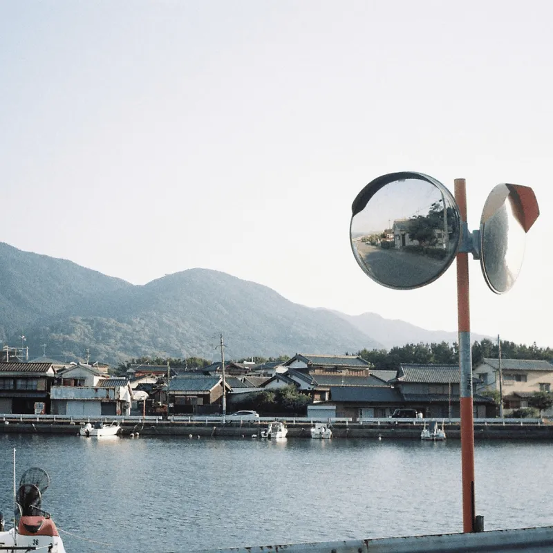 A canal in Itoshima with the mountain in the background, and a traffic reflector in the foreground